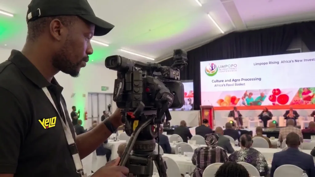 Camera operator filming a panel discussion at the Limpopo Investment Conference, with delegates seated in front of a large stage screen